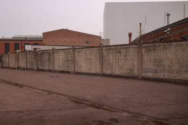 Binanın önünde beton çitli tuğla duvar. Çit yüksek ve duvar tuğladan yapılmış.