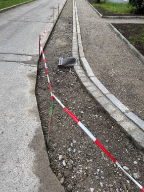 Kırmızı ve beyaz şeritli bir bariyer ve drenaj ızgarası olan bir yol. Bariyer, insanların sınıra çok yakın yürümesini engellemek için yolun kenarına konur.