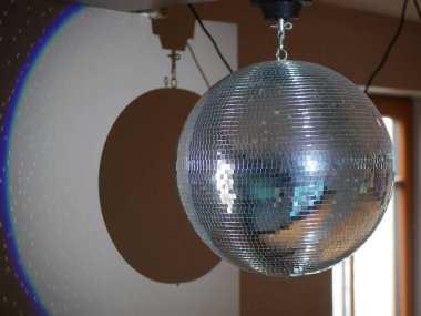 Gümüş disko topu tavandan sarkıyor. Topun ışığı duvara yansıyor ve renkli ve eğlenceli bir atmosfer yaratıyor.