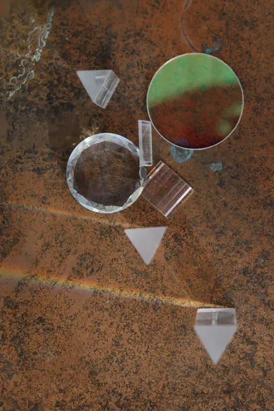 Bir üçgen, bir kare ve bir daire de dahil olmak üzere cam nesneler kahverengi bir yüzeye yerleştirilmiştir. Nesneler farklı şekil ve boyutlarda görünüyor.