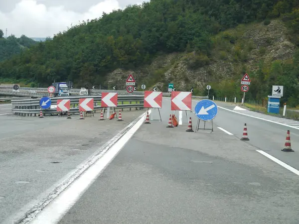 Bir sürü turuncu koni ve tabela olan bir yol. Yol kapalı ve yerde mavi bir ok var.