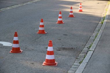 Bir sıra turuncu ve beyaz trafik konileri bir caddede dizilmiştir. Külahlar sıralanır, bazıları öne doğru, bazıları da arkaya doğru.... .