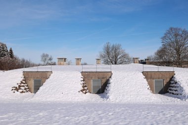Karla kaplı çatısı olan üç küçük bina. Binaların çatısına yığılan kar, onlara rahat ve kırsal bir görünüm kazandırıyor. Binalar karlı bir arazide yer alıyor.. .
