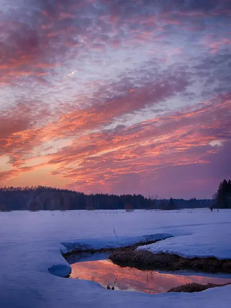 Gökyüzünün renklerini yansıtan bir nehirle karlı bir arazide güzel bir gün batımı..