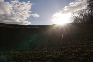 Üzerinde parlak bir güneş parlayan bir yamaç. Güneş çimlerin üzerine gölge düşürüyor