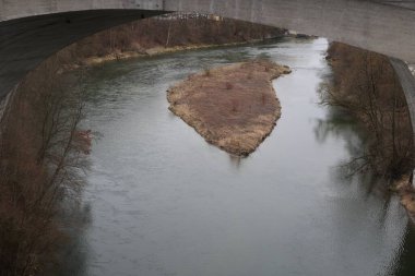 Üzerinde köprü olan bir nehir ve ortasında küçük bir ada. Su sakin ve gökyüzü bulutlu.