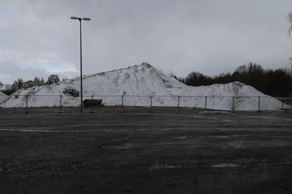 Tepede büyük bir kar yığını var. Arkasında çit var. Kar derindir ve tüm tepeyi kaplar. Huzurlu ve huzurlu bir atmosfer yaratır. Çit uzak bir yerde.