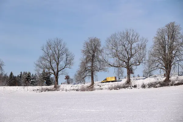 Sarı bir kamyon bir tarlada karlı bir yolda ilerliyor. Ağaçlar çıplak ve gökyüzü temiz. Huzurlu ve huzurlu bir sahne.. .