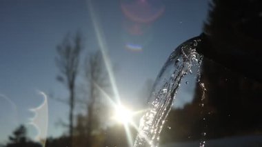 Su akıntısı bir musluktan akıyor, arka planda güneş ışıl ışıl parlıyor. Sahne huzurlu ve sakin, su rahatlatıcı bir etki yaratıyor.