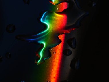 Gökkuşağı, karanlık bir yüzeydeki su damlacıklarına yansıyor. Gökkuşağının renkleri canlı ve su damlacıkları küçük ve dağınık. Merak ve güzellik kavramı