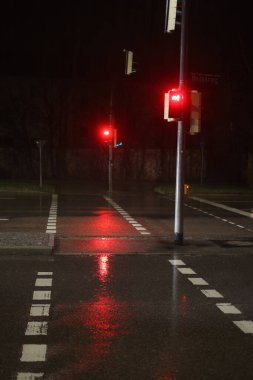 Sokaklar ıslak ve trafik ışıkları kırmızı. Işıklar kutuplara yerleştirilmiş ve iki caddenin kesiştiği yerde.. .
