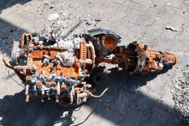 Paslı bir motor yerde, etrafında bir sürü enkaz var. Motor eski ve çok yıpranmış durumda. Olay yeri ıssız ve terk edilmiş.