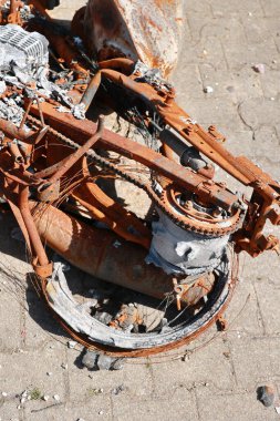 Paslı bir motosiklet yerde ve zinciri kayıp. Motosiklet bakımsız durumda ve görünüşe göre yangın çıkmış.