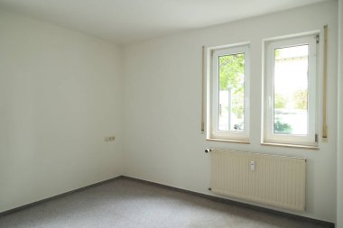 Penceresi ve radyatörü olan bir oda. Oda boş ve minimalist bir görünüşü var.