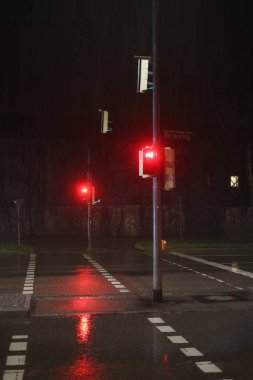 Kırmızı iki trafik lambası olan bir cadde. Sokaklar ıslak ve ışıklar yağmuru yansıtıyor.. .