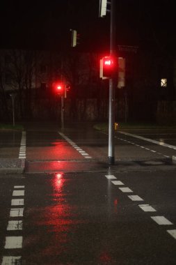 Islak bir sokakta iki trafik ışığı olan yağmurlu bir gece. Işıklar kırmızı, ya yolun kapalı olduğunu ya da sürücülerin durması gerektiğini gösteriyor. Sokak da ıslak, bu da kaygan olabilir.. .