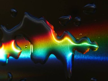 Gökkuşağı su birikintisine yansıyor. Renkler canlı ve su damlacıkları görüntünün her tarafına dağılmış.