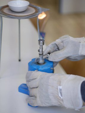 Üzerinde beyaz etiket olan mavi bir nesne tutuyor. Nesne bir laboratuvar ortamında kullanılıyor