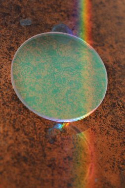 Üzerinde gökkuşağı yansıması olan yeşil bir daire. Çember kahverengi bir yüzeyde.
