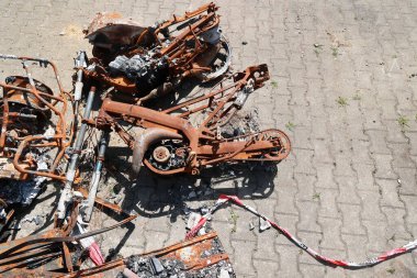 Paslanmış motosiklet parçaları ve kırmızı beyaz bir ip. Sahne kaotik ve düzensiz. Motosiklet parçaları yere saçılmış.