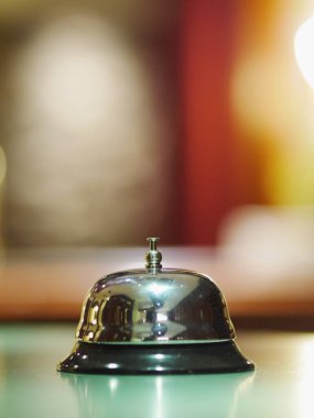 Gümüş çan masanın üzerinde duruyor. Zil parlak ve siyah bir tabanı var. Masa yeşil ve oda loş ışıklı.