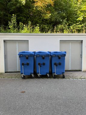 Etkili kentsel atık yönetimi çözümleri sunan bir binanın yanına düzgün bir şekilde yerleştirilmiş üç mavi çöp kutusu