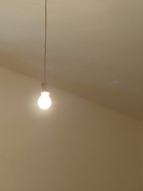 Tavandan sarkan tek bir ampul. Ampul beyaz ve odadaki tek ışık kaynağı.