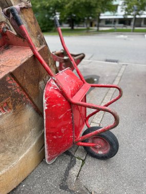 Çekici bir klasik kırmızı el arabası, aşınmasını ve tarihini gösteriyor, şehir manzarasında yıpranmış bir duvara dayanıyor.