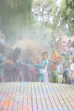 Lviv, Ukrayna - 18 Temmuz 2021: Renkli Holi Festivali, yetişkin ve küçük çocuklardan oluşan bir kalabalık renkli boya atıyor. Kızılderili tatili, çocuklar tahta sahnede koşuyor.