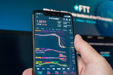 FTX logolu telefonu tutan adam. Şifreleme grafiğinin küresel düşüşü - FTT jetonu uygulama ekranındaki dosya şifreleme borsasına düştü. FTX iflası ve jetonun değer kaybı.