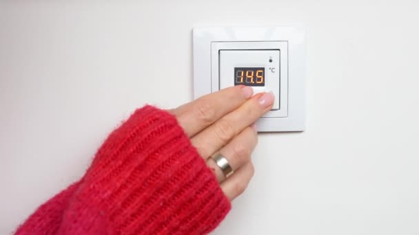 床暖房制御パネルの赤いセーター設定温度で女性の手 凍結女の子は壁に床暖房サーモスタットパネルのボタンを押すことによって部屋の温度を上げる — ストック動画