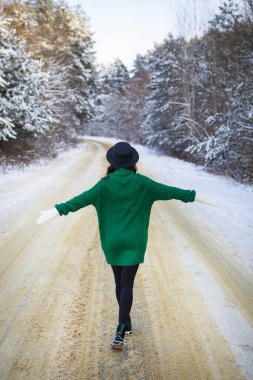Yeşil kazaklı ve şapkalı genç bir kız sık bir çam ormanında karlı bir yolun ortasında yürüyor. Dondurucu gün