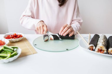 Suşi yaparken kız farklı aromalı suşi yapar. Taze somon, havyar, avokado, salatalık, zencefil, pirinç. Yuvarlamayı parçalara ayır.