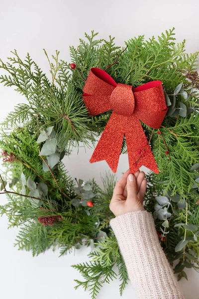 Stylish Christmas wreath for the interior, hang the wreath on the door. Handmade, the girl is holding a freshly made wreath with a beautiful red bow. Festive atmosphere