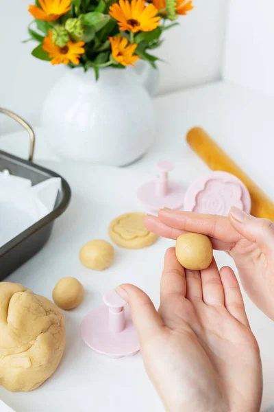 Preparing the dough for making cookies with molds in the form of flowers, a rolling pin, a bouquet of orange flowers and a baking sheet, the girl forms cookies in her hands. Concept of family and cooking