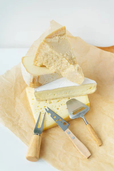 Different types of cheese lie on top of each other with cheese knives on parchment. A delicious delicacy. Vertical photo