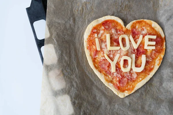 Italian heart shaped pizza with salami, tomato sauce, parmesan, pizza sauce, mozzarella and olive oil on parchment paper with cheese I love you. Love concept for Valentine\'s Day February 14