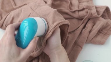 Female hands with shaver cut wool cloth. A young woman using a portable razor on shorts - device to remove pellets and lint. Girl caring for clothes with a fluff trimmer for longer use of clothing. 4k