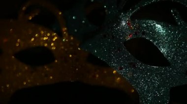 Two luxury traditional venetian masks on dark background illuminated and sparkles from the darkness. Blue and gold shiny carnival masquerade fantasy mask with small colorful stars under light in dark