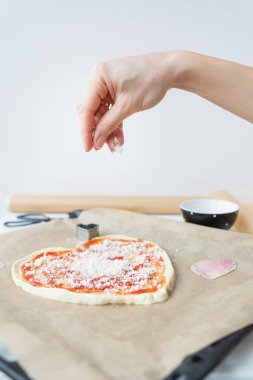 Kalp şeklinde pizza hamuru, şef pizzaya parmesan peyniri serper. Sevgililer Günü için sürpriz konsepti