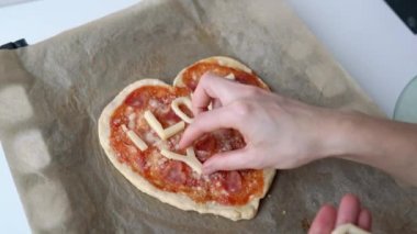 Kadın eli peynirin yazısını hazırlıyor. Seni seviyorum. İtalyan kalbi şeklinde pizza, salam, domates sosu, parmesan sosu, sos, mozzarella ve parşömen kağıdında zeytinyağı. Aşk konsepti