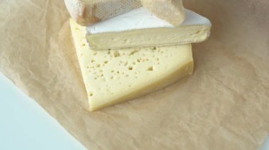 Medium hard cheese heads brie, parmesan on craft paper. Pile pieces of different kinds handmade cheese stacked in vertical row on wooden table with cheese fork on top - healthy organic eating concept