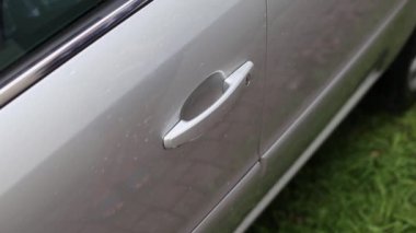 Gri araba kapısını açan sıska, genç bir kadın eli. Kadın sürücü hafta sonu araba sürmeden önce arabanın kapısını açar. Sokakta üzerinde çimen olan gri hatchback aracına anahtarsız erişim - sinematik görüntüler
