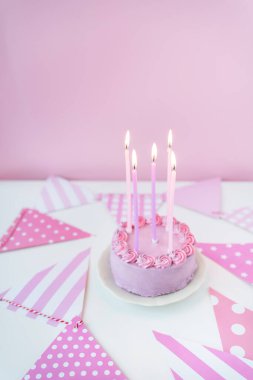Parti bayraklarının pembe arka planında, tabakta pembe lavantalı bento keki, kekin üzerinde yanan mumlar. Kutlama, mutlu bir gün
