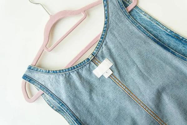 Denim clothes on a hanger. White label on denim clothes with size and brand, place for writing, mockup. Close-up