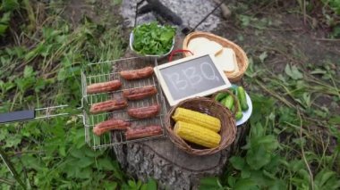 Buharda pişmiş sosis, kızarmış tost yanında mısır ızgarası ve alevlerin yanında salata. Arkadaşlar barbekü partisini arka bahçede yaparlar. Yaz günü açık havada ahşap tahtayla ızgara yiyeceklerin manzarasını kapat.