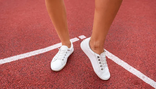 Red plastic coating on the playground, the legs of a girl in white sneakers. Preparing for the competition