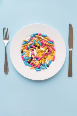 Tabletler, kapsüller, vitaminler ve mavi zemin üzerinde beyaz bir tabakta doğal organik gıda takviyeleri. Minimum modern eczane ya da sağlık hizmeti konsepti. Dikey fotoğraf
