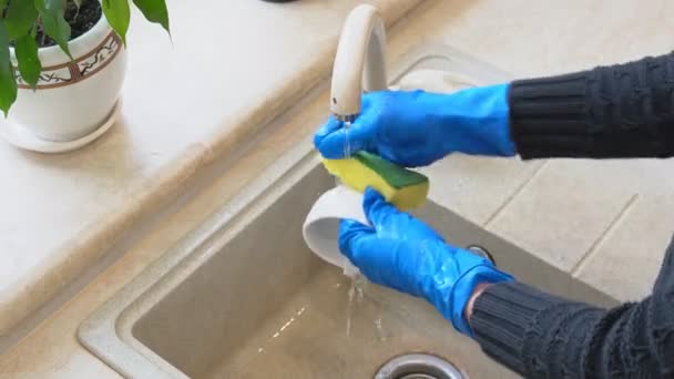 メイドは家の台所のセラミックシンクの青ラテックス手袋洗浄皿を室内で着用するスポンジを使用します 到着後は家事労働者の女性がコーヒーカップを洗う 家事をする主婦の女の子 — ストック動画