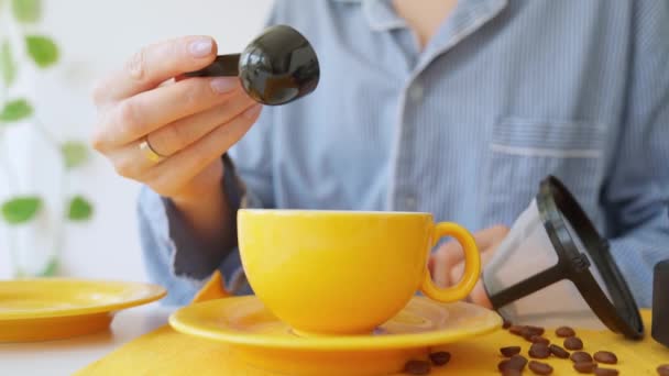 黄色のカップにコーヒー豆を注ぐ少女の手の閉鎖 黒豆をゆっくりとボウルにコーヒースプーンの秋 女の子はコーヒーメーカーでコーヒーを作る準備をしている Fps — ストック動画